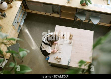 Giovane donna adulta che scolpisce la ceramica di argilla al tavolo dell'officina all'interno Foto Stock