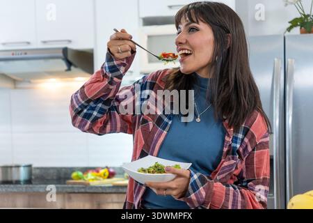 Donna in cucina che si gode un piatto di insalata fresca e sana Foto Stock