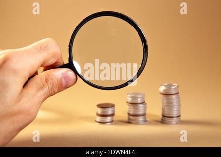 Lente d'ingrandimento e monete su sfondo marrone. Business e finanza. Foto Stock