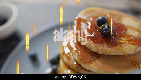 Versare sciroppo d'acero su una pila di pancake dorati su un piatto grigio opaco sul piano portapaziente, con mirtilli Foto Stock