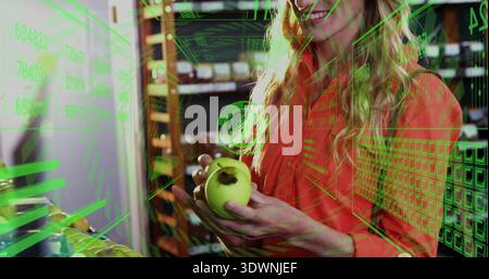 In possesso di una mela verde donna adulta che indossa la parte superiore arancione che controlla la sezione prodotti presso il punto vendita con HUD AR Foto Stock