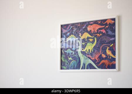 Camera luminosa con parete bianca decorata con un puzzle a tema dinosauro. La luce del sole che scorre attraverso la finestra si riflette sui colori Foto Stock