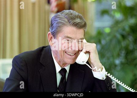 Questa fotografia del 1987 cattura il presidente Ronald Reagan nell'ufficio ovale, sorridendo calorosamente mentre parla al telefono. Reagan, vestito con un vestito e una cravatta, appare impegnato e rilassato durante la conversazione, probabilmente una chiamata diplomatica con un leader mondiale. Foto Stock