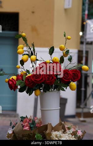 Vivace bouquet di rose rosse mescolate con limoni gialli freschi in un vaso bianco in una bancarella della città vecchia di Nizza, Francia. Nizza, Francia Foto Stock