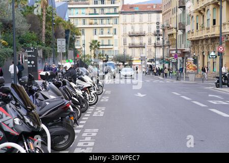 Lunga fila di scooter colorati parcheggiati lungo un vivace viale urbano di Nizza, incorniciati da eleganti edifici Belle Époque e palme Foto Stock