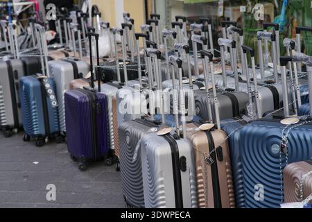 File di luccicanti valigie rigide in argento, blu, viola e rosa riempiono il marciapiede all'esterno di un vivace negozio di valigie a Vieux Nice, Francia. Foto Stock