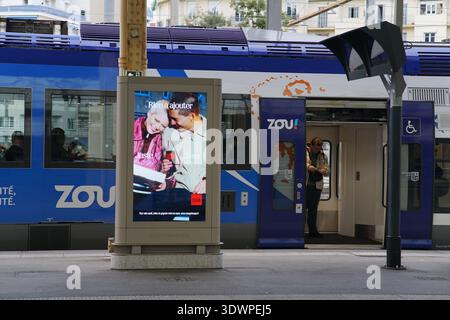 Il vibrante cartellone pubblicitario della stazione ferroviaria di Nizza promuove il "Plaisir d'hiver" di Zou con una gioiosa coppia di anziani che sorseggia bevande calde Foto Stock