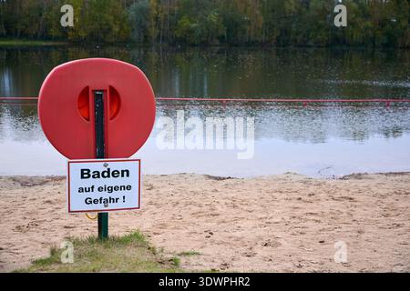 Un importante banco di salvataggio rosso con un "Baden auf eigene Gefahr!" (Fare il bagno a proprio rischio!) l'insegna si trova su una spiaggia sabbiosa di un lago. L'acqua calma si riflette Foto Stock