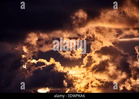 Un cielo mozzafiato e suggestivo al tramonto, pieno di nuvole spesse e scure illuminate dalla luce dorata e arancione. I raggi del sole penetrano attraverso le fessure i Foto Stock