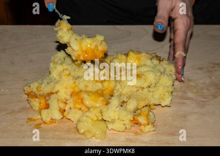 Sciogliendo il cibo confortevole in azione: Purea cremosa di patate mescolata con un ricco formaggio fuso, catturata in un caldo momento di cucina autentica. Visuale perfetta Foto Stock