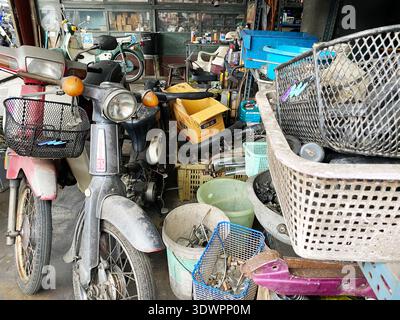 Phuket, Thailandia - 28 ottobre 2025: Due motociclette d'epoca sono parcheggiate in un garage disordinato pieno di attrezzi, cesti e pezzi di ricambio sparsi Foto Stock