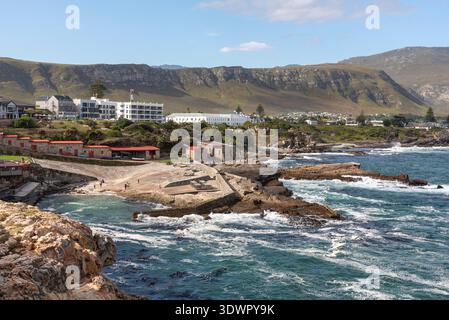 Hermanus, Sudafrica. 14.02.2026. Una vista panoramica di un villaggio sul mare caratterizzato da un'architettura tradizionale accoccolata sullo sfondo di colline ondulate a. Foto Stock