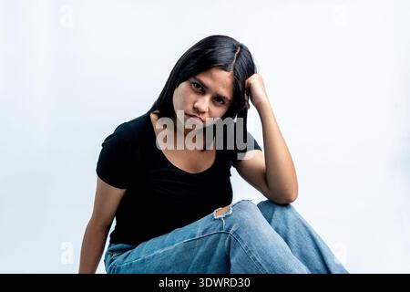 Una giovane donna del sud-est asiatico in abiti casual seduta su sfondo bianco, che sembra stressata e premurosa con la mano sulla testa. Foto Stock