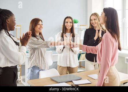 Due giovani donne d'affari stringono la mano mentre i membri del team applaudono Foto Stock