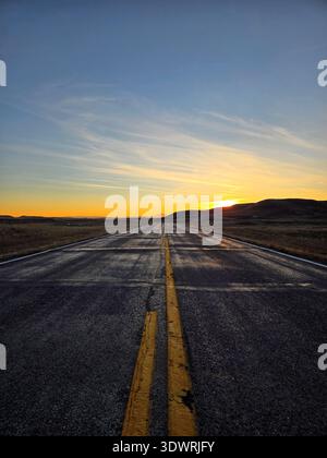 Su un'autostrada vuota, diretta verso il tramonto, all'orizzonte si trova un cielo arancione scintillante. Vista ad angolo ridotto dell'asfalto, con linee gialle doppie e singole . Foto Stock