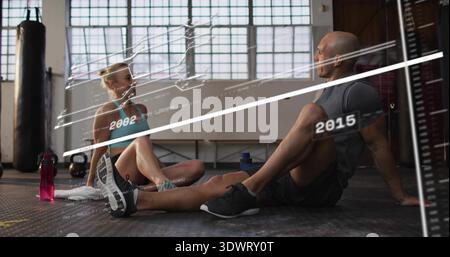 I partner di allenamento riposano seduti sul pavimento della palestra, indossando un reggiseno sportivo, mostrando una bottiglia rosa e un rivestimento Foto Stock