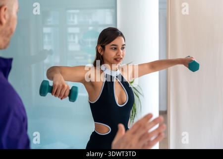 Giovane donna che fa esercizi di fisioterapia con manubri Foto Stock