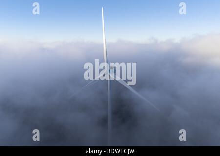 Vista aerea di una sola turbina eolica avvolta da una mistica coperta di nebbia, il suo bianco intenso che contrasta con la morbida ed eterea nebbia, Windpark Freilä Foto Stock