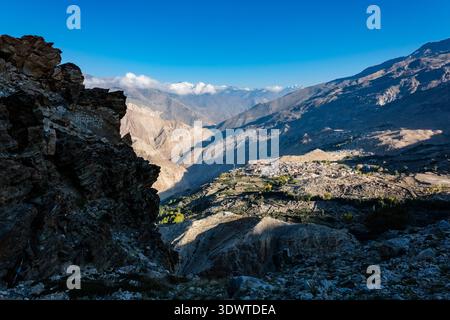 Visto da un'alta cresta rocciosa, il villaggio di Nako sorge all'interno di una vasta e arida valle di montagna sotto un cielo azzurro e limpido in lontananza. Foto Stock