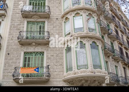 La facciata dell'edificio di appartamenti modernista catalano di Barcellona presenta finestre a bovindo ornate, persiane verdi e una bandiera Estelada che fa riferimento al 2017 Foto Stock