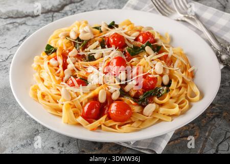 Fettuccine con fagioli bianchi, pomodori ciliegini e spinaci da vicino in un piatto sul tavolo. Orizzontale Foto Stock