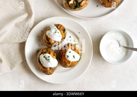 Deliziose patate al forno ripiene con funghi, spinaci, cipolle caramellate, formaggio cheddar e salsa a base di yogurt su un piatto bianco su un dorso di pietra leggera Foto Stock