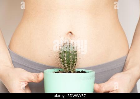 Un cactus in vaso sullo sfondo dello stomaco di una ragazza sul tema del dolore allo stomaco, dolore acuto Foto Stock