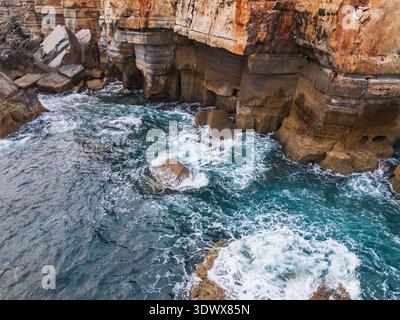 Vista aerea con droni delle onde turchesi dell'oceano che si infrangono contro scogliere scoscese e formazioni rocciose sulla costa del Portogallo. Foto Stock