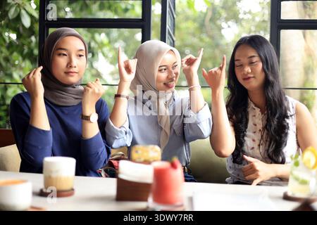 Tre belle e felici giovani donne asiatiche sedute al tavolo chiacchierando giocando con il cellulare nel bar o nel ristorante, creando contenuti per Soci Foto Stock
