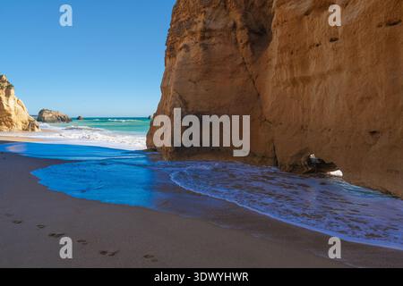 Le scogliere calcaree illuminate dal sole incorniciano una tranquilla spiaggia sabbiosa mentre le onde turchesi dell'Atlantico si riversano a riva nell'Algarve, Portogallo. Foto Stock