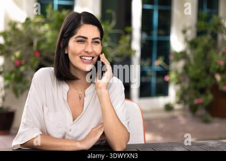 Felice giovane donna latina che parla al cellulare fuori Foto Stock