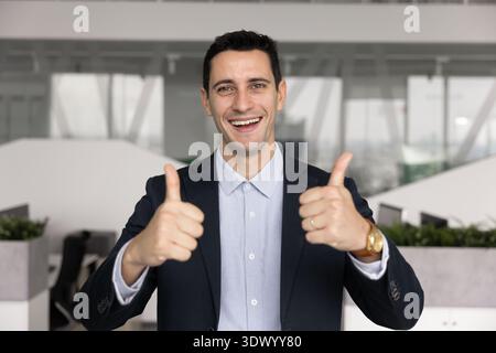 Un dirigente maschile ispanico di successo che guarda la fotocamera che tiene i pollici in alto Foto Stock
