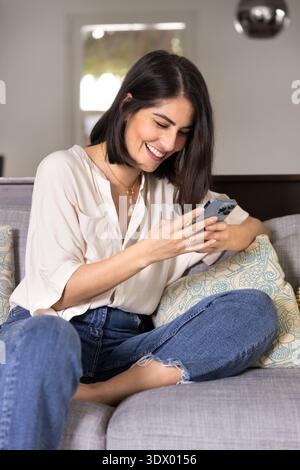 Felice giovane ispanica donna che guarda contenuti divertenti sullo smartphone Foto Stock