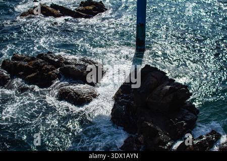 Onde che si infrangono contro le rocce costiere Foto Stock
