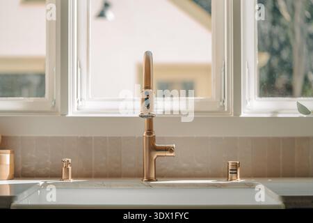 Primo piano di rubinetti da cucina in ottone e lavabo in grembiule in una cucina residenziale moderna e luminosa. Foto Stock