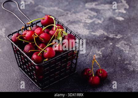 Ciliegie rosse dolci fresche nel cestello su fondo scuro, fuoco selettivo Foto Stock