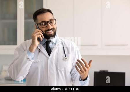 Sorridente medico di sesso maschile che parla al telefono nel posto di lavoro dell'ospedale Foto Stock