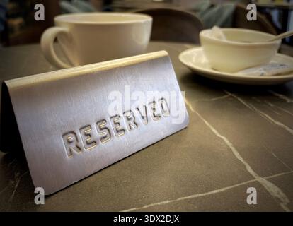 Placca in metallo riservata in piedi sul tavolino da caffè con sfondo sfocato, atmosfera accogliente del ristorante e luce soffusa del cinema Foto Stock