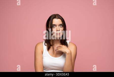 Giovane donna che posa, mostra un'espressione goffa e dubbiosa, si sente sconcertata o fa una giocosa grimace Foto Stock