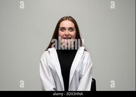 Una giovane donna che fa un'espressione facciale divertente e giocosa, si sporge la lingua, mostra umorismo e sciocchezza Foto Stock