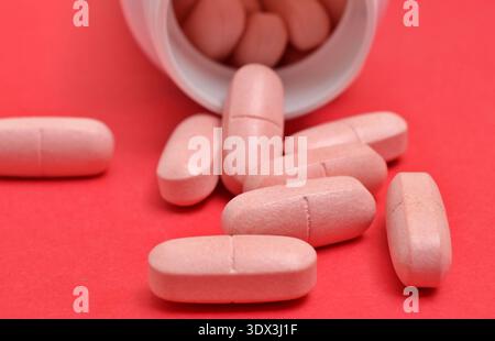 Le compresse oblunghe rosa fuoriescono da un flacone bianco aperto di plastica per medicinali Foto Stock