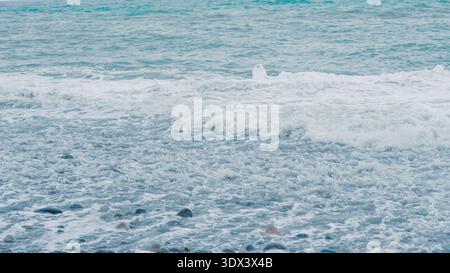 Le onde si infrangono dolcemente su una costa rocciosa con ciottoli visibili sotto l'acqua cristallina Foto Stock