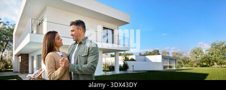 Felice sorridente coppia di mezza età nuovi acquirenti di proprietà in piedi fuori casa. Foto Stock