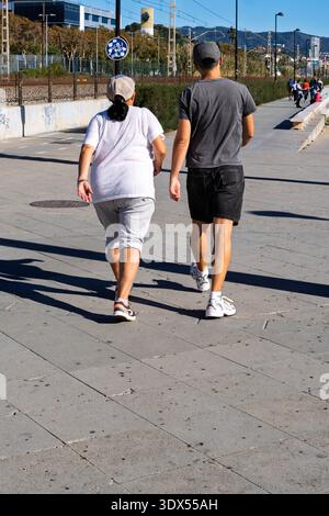 Un uomo e una donna in abbigliamento sportivo camminano lungo un sentiero lastricato sul mare durante una mattinata di sole. Foto Stock
