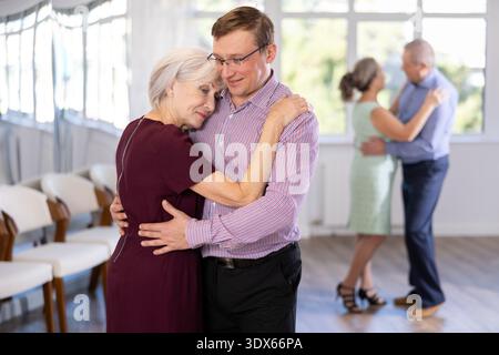 Uomo e donna senior felici che ballano in sala da ballo lenta durante le lezioni di gruppo in studio Foto Stock