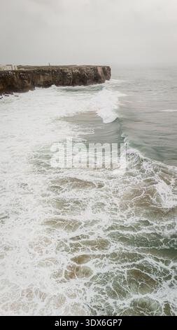 Il drone cattura una splendida vista aerea delle potenti onde dell'Oceano Atlantico che si infrangono contro le scogliere rocciose di una pittoresca spiaggia in Portogallo, vetrina Foto Stock