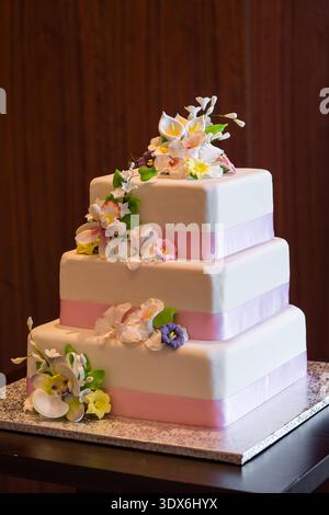 Torta nuziale a più piani decorata con fondente bianco, nastro rosa e delicati fiori di zucchero. Foto Stock
