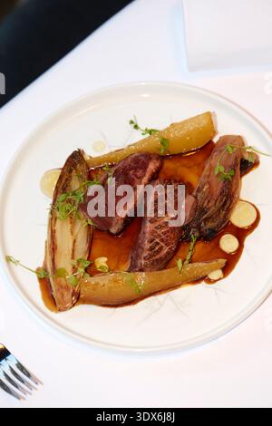 Un piatto gourmet splendidamente placcato con carne succulenta abbinata a vivaci verdure caramellate, guarnite con erbe fresche, elegantemente arredate Foto Stock
