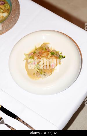 Un piatto gourmet caratterizzato da capesante perfettamente placcate, guarnite con verdi, elegantemente presentato su una tovaglia bianca con finissima argenteria in un alto Foto Stock