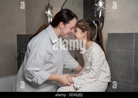 Una madre amorevole e sua figlia condividono un momento tenero in bagno, mostrando il loro stretto legame e affetto. La dinamica familiare è calda e sentita Foto Stock